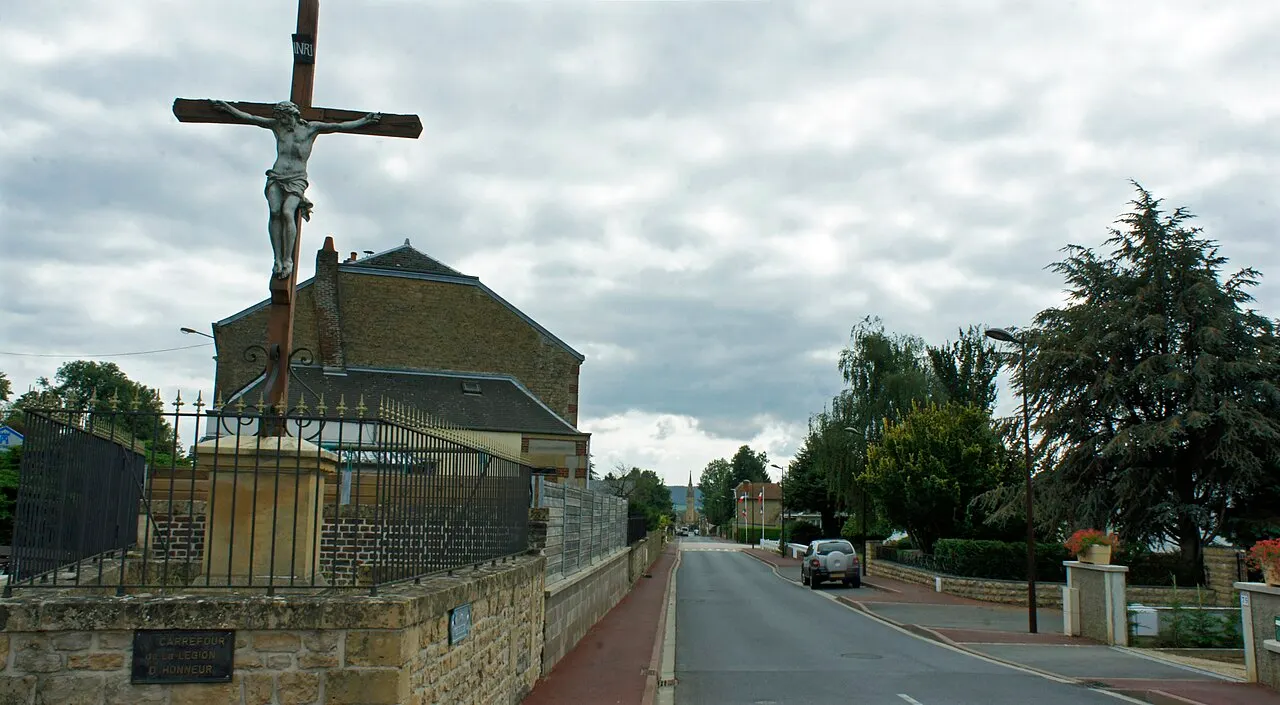 Vue d'une croix de chemin et de la Perspective de la rue Gambetta à Bazeilles, au fond, l'église.