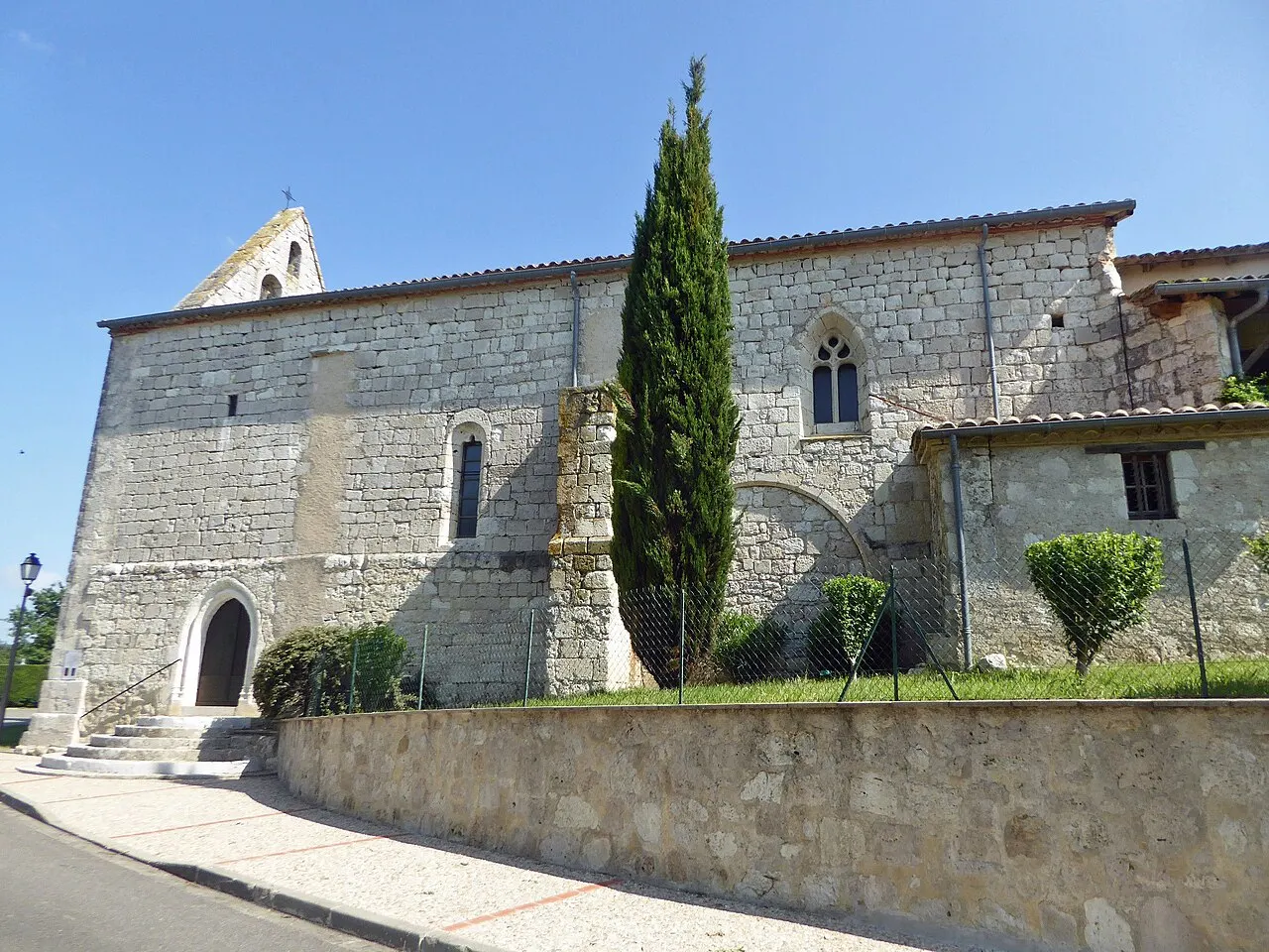 Eglise haute et massive en pierres claires percée de petites ouvertures en arc brisé, clocher mur en façade